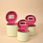 Tres neceseres circulares de color crema con textura geométrica, tapas abiertas revelando interior rosa y espejo rectangular integrado.