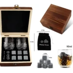 Cofre de madera con dos copas de whisky, seis piedras de enfriamiento y bolsa de tela negra; incluye medidas visibles y muestra bebida servida con hielo.