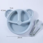 Plato infantil de fibra de trigo en color gris claro, con forma de oso y tres compartimentos. Incluye cuchara y tenedor con texto visible. Medidas: 20 cm de diámetro, 7 cm de altura y 4.5 cm de profundidad.