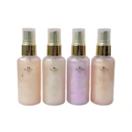 Cuatro botellas de spray iluminador corporal Paulis en tonos nude, blanco, lavanda y rosa pálido, con pump dorado y etiqueta frontal con logotipo y nombre del producto.