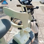 Silla infantil delantera para scooter en color crema, con respaldo ergonómico, asiento acolchado y arnés de seguridad ajustable. Instalada sobre el manillar, permite al niño viajar frente al conductor con visibilidad directa.