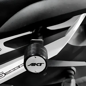 Vista cercana del slider trasero Akt Dynamic en acero inoxidable, montado en la parte inferior de una moto, con acabado metálico brillante y logotipo visible.