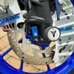 Sliders Spool MT 15 de acero inoxidable instalados en rueda delantera azul, protegen chasis de impactos y arañazos.