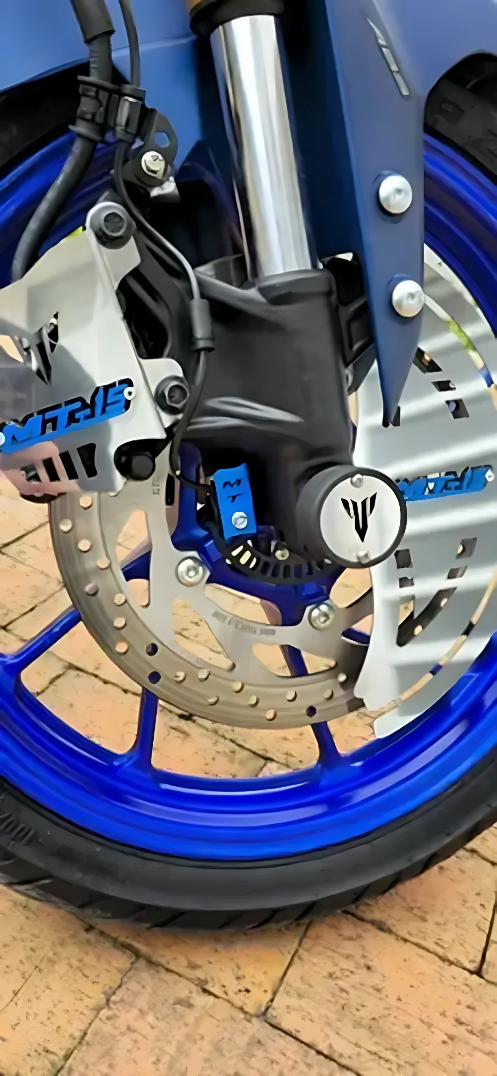 Sliders Spool MT 15 de acero inoxidable instalados en rueda delantera azul, protegen chasis de impactos y arañazos.