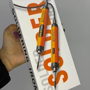 Soldador portátil Sk-1 en caja blanca con letras naranjas, mostrando dos puntas intercambiables y cable negro; incluye estano.