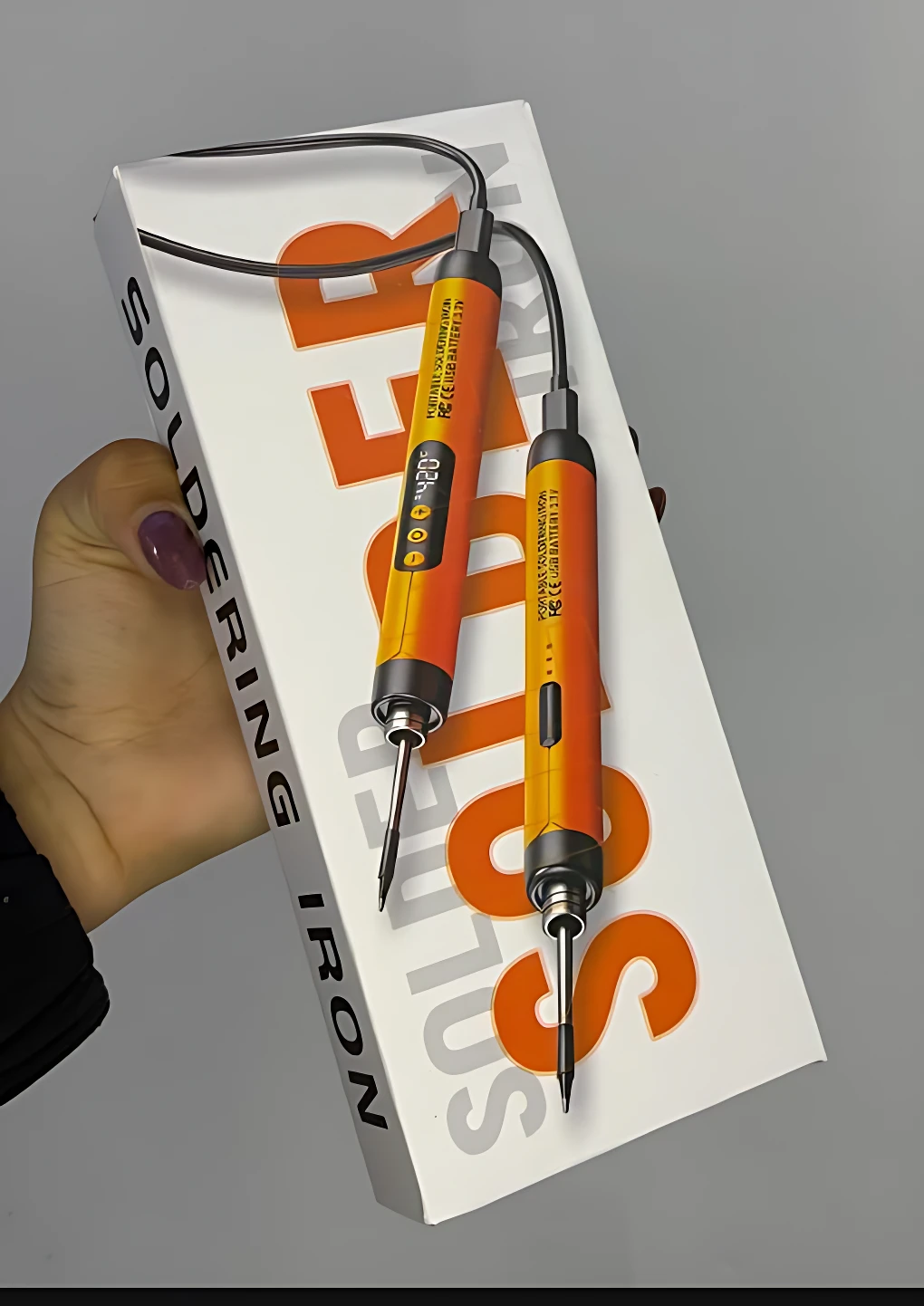 Soldador portátil Sk-1 en caja blanca con letras naranjas, mostrando dos puntas intercambiables y cable negro; incluye estano.