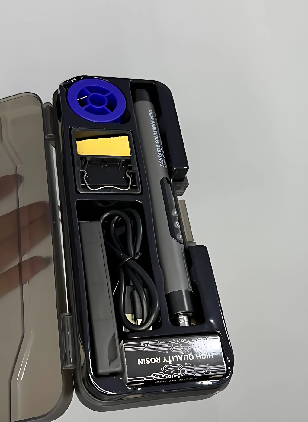 Caja de soldador portátil Sk-1 abierta mostrando estano, cable USB, esponja de limpieza y base de carga en interior negro.