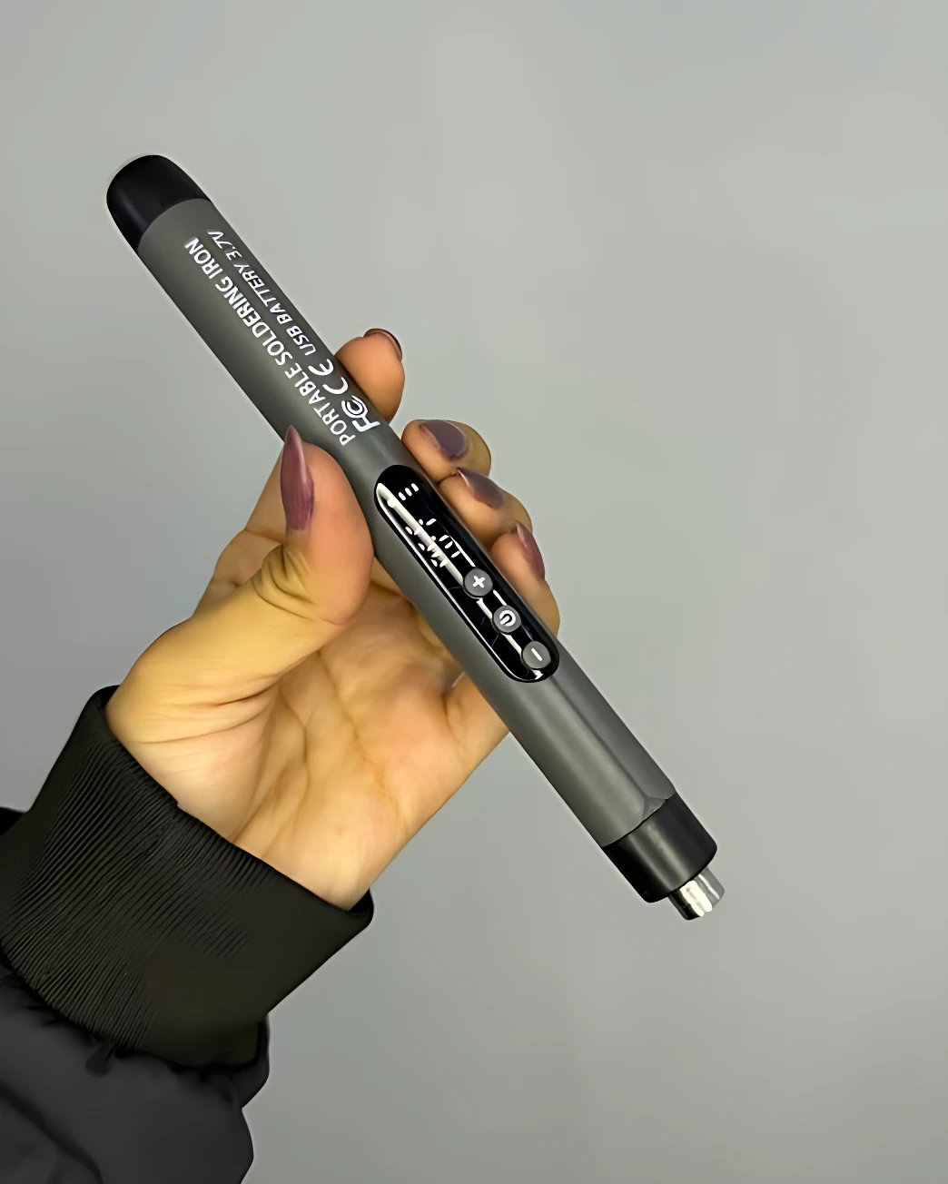 Soldador portátil Sk-1 en mano, cuerpo gris metálico con punta de soldar visible y estano incluido en la punta.