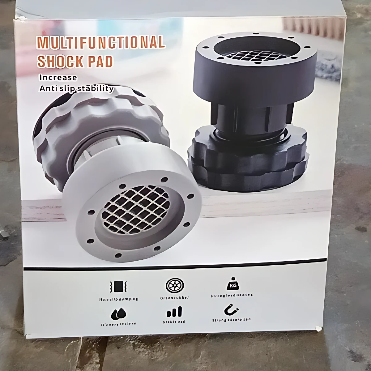 Caja de soporte para patas de lavadora, color negro y gris, con diseño antideslizante y amortiguador de impacto. Incluye dos unidades, visibles en la caja.