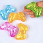 Cinco juguetes antiansiedad en forma de control de videojuegos, colores azul, amarillo, rosa y verde con brillo interior, uno sostenido en mano.