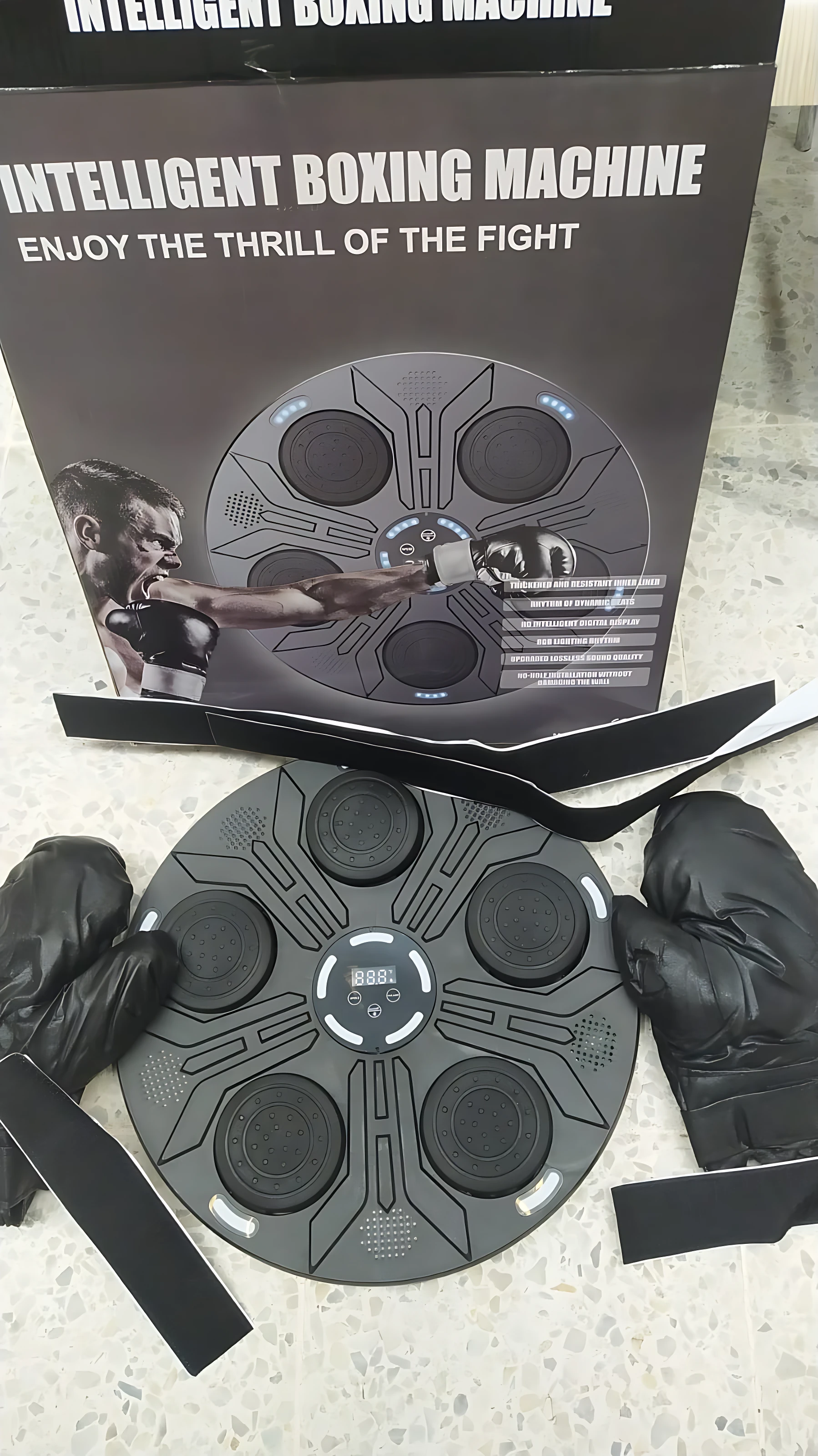 Tablero de boxeo negro con guantes y correas, junto a su caja que muestra de entrenamiento.