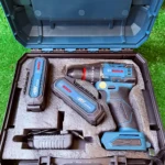 Taladro inalámbrico Bosch 12V con baterías y cargador en estuche azul sobre césped artificial.