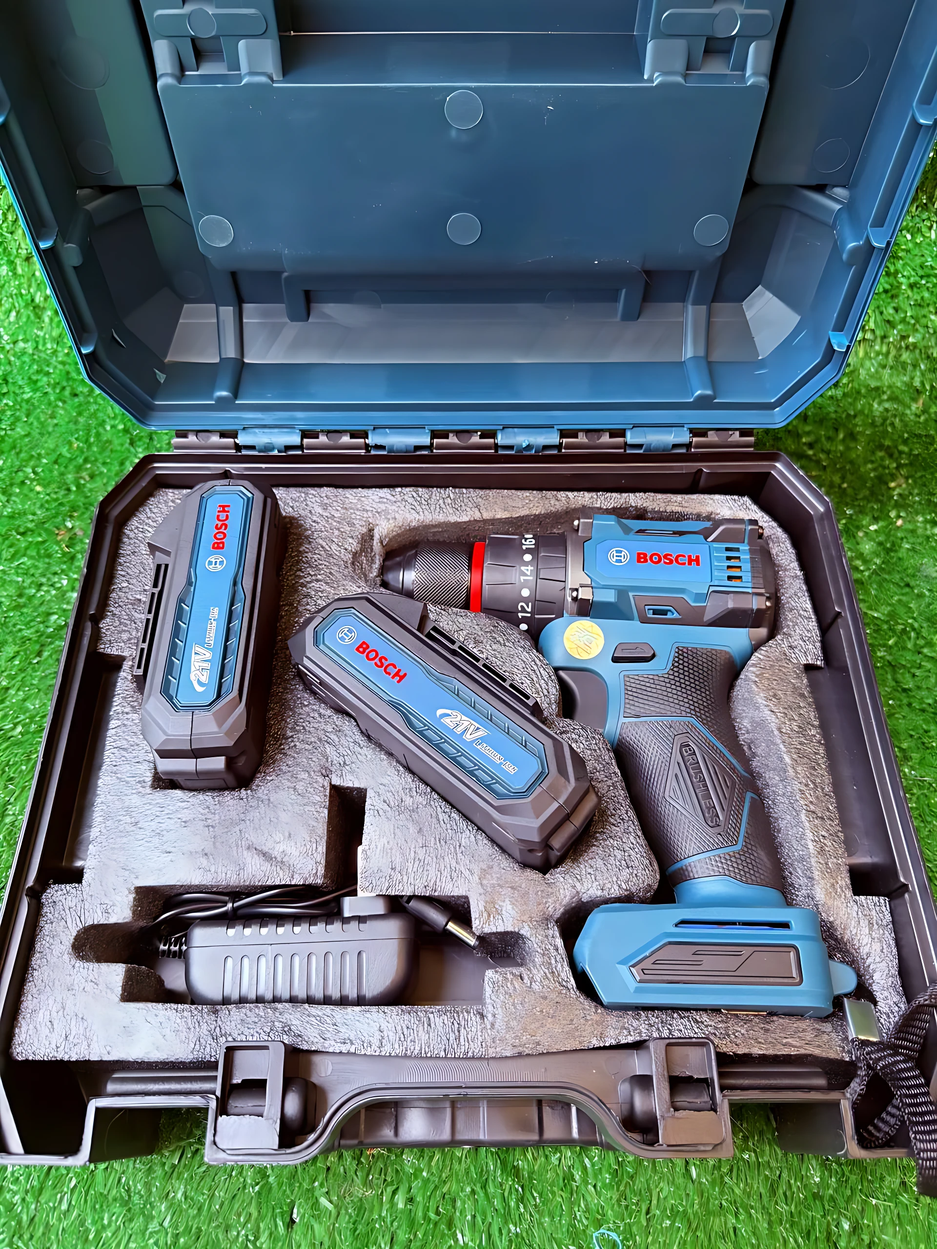Taladro inalámbrico Bosch 12V con baterías y cargador en estuche azul sobre césped artificial.
