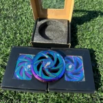 Tapa magneto rotor NKD con acabado iridiscente, mostrando tres piezas de color azul y morado sobre caja negra y su empaque original con espuma protectora.
