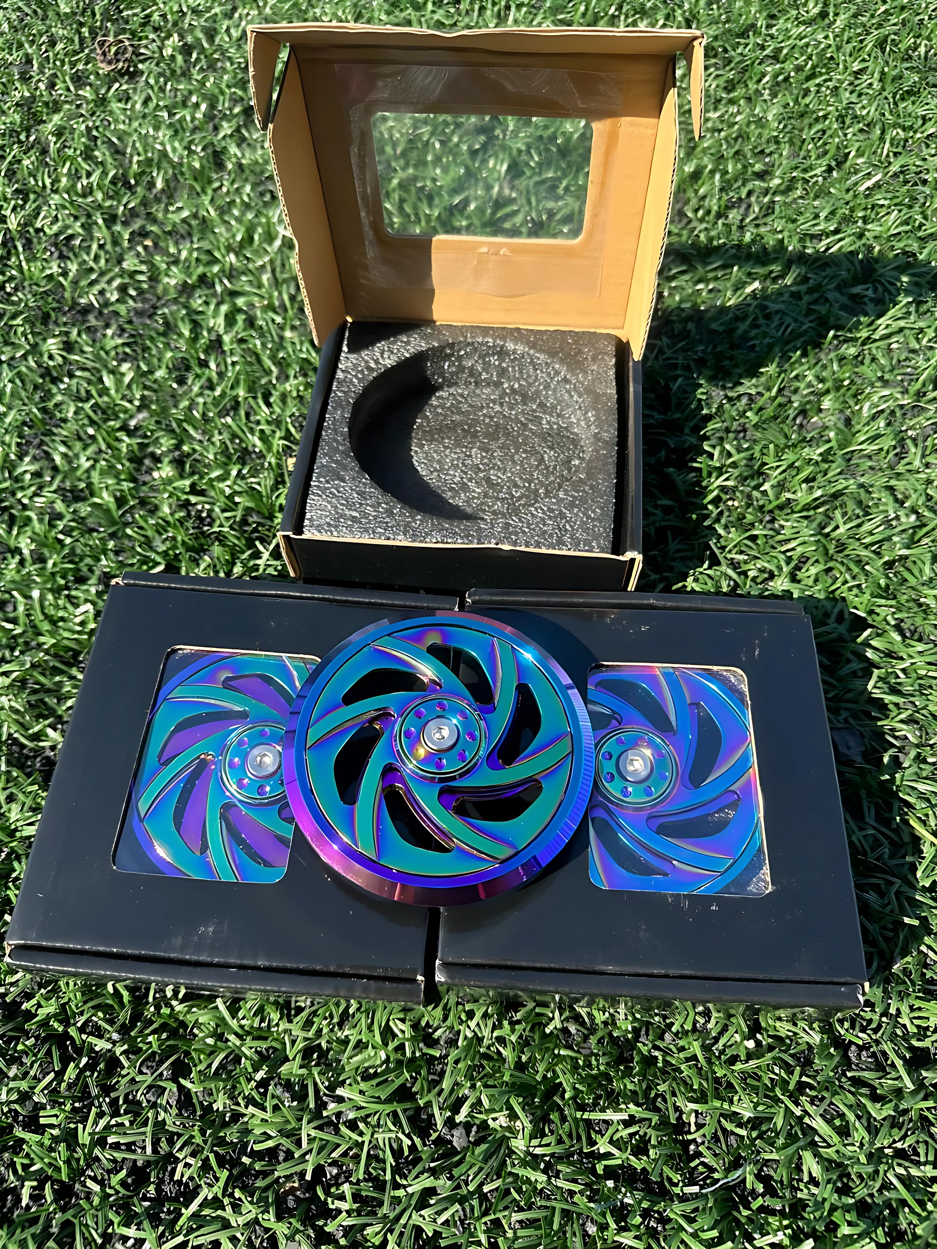 Tapa magneto rotor NKD con acabado iridiscente, mostrando tres piezas de color azul y morado sobre caja negra y su empaque original con espuma protectora.