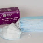 Caja morada de tapabocas quirúrgicos de tres capas, color azul claro, con 50 unidades. Se muestra una unidad desplegada al frente y un montón de tapabocas doblados detrás.