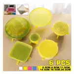 Set de 6 tapas de silicona elásticas amarillas de 6.5 a 20.5 cm para sellar platos y recipientes, dispuestas sobre una superficie de madera.