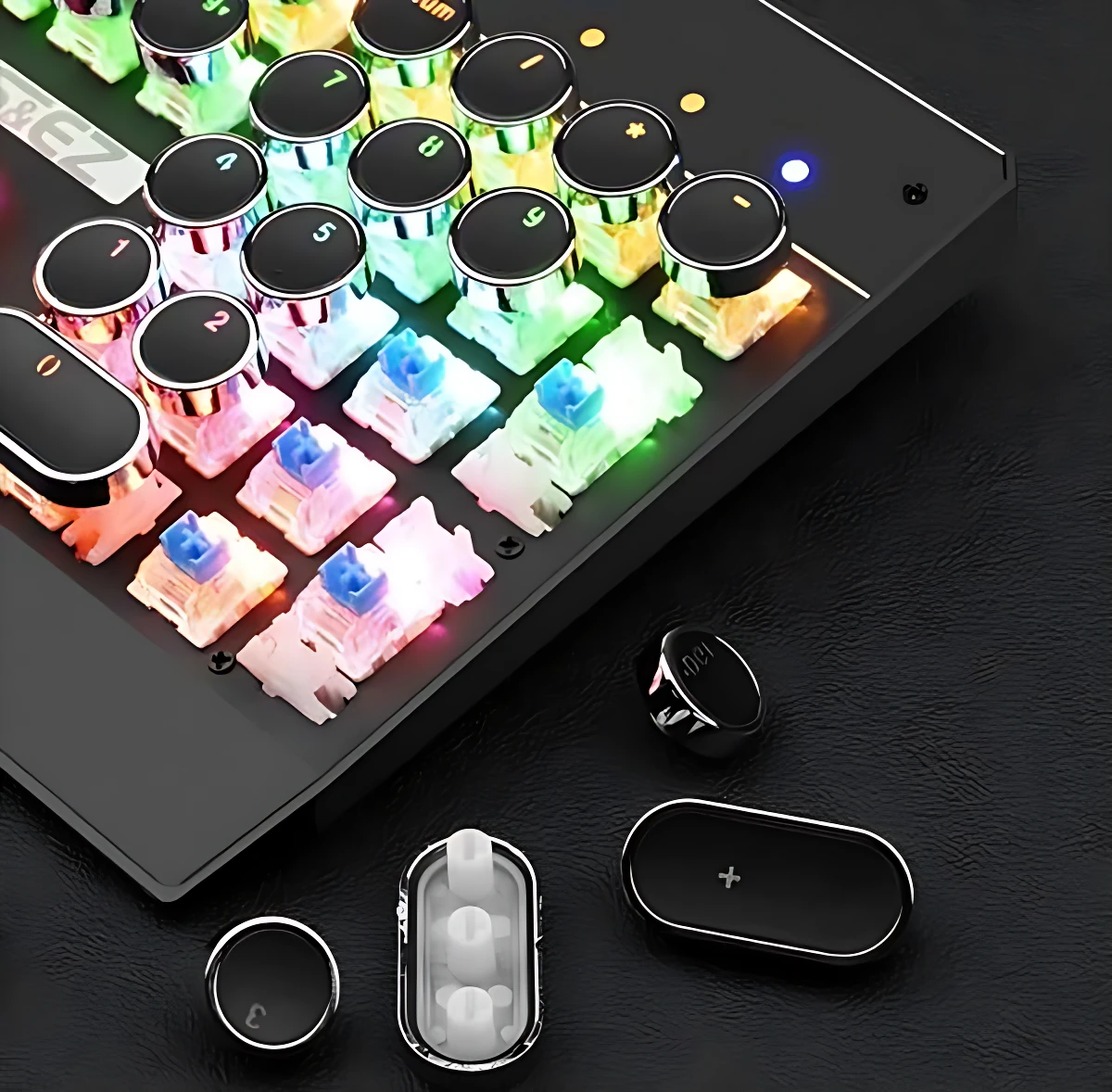 Teclado mecánico negro con teclas redondas J, switches RGB multicolor y accesorios incluidos, sobre superficie oscura.