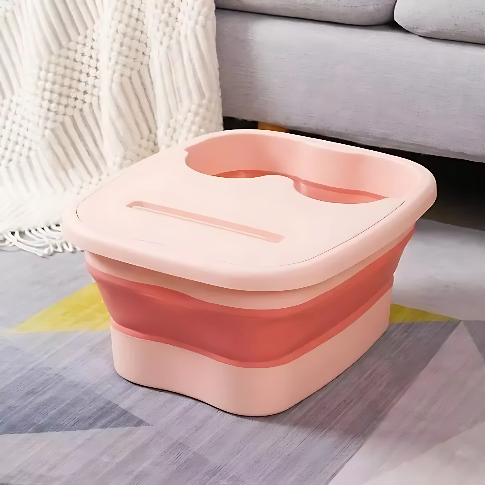 Tina spa plegable rosa con rodillos masajeadores, tapa con ranura y base colapsable, sobre alfombra geométrica en interior.