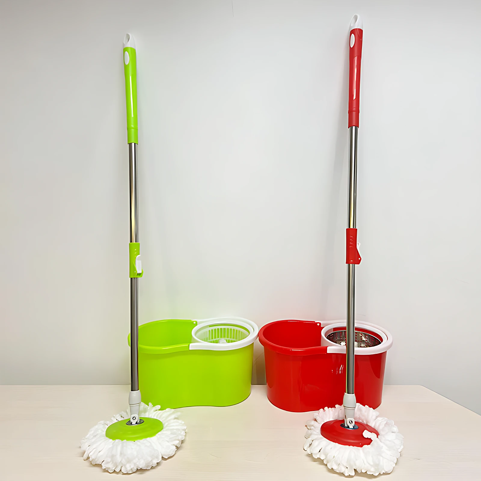 Dos traperos mágicos con cabezal giratorio y escurrido automático, uno verde y otro rojo, junto a sus respectivos cubos de plástico con sistema de escurrido integrado, sobre superficie clara.