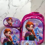 Kit escolar fucsia con diseño de Frozen, incluye morral grande, lonchera, cartuchera, lápices y regla sobre superficie de mármol.