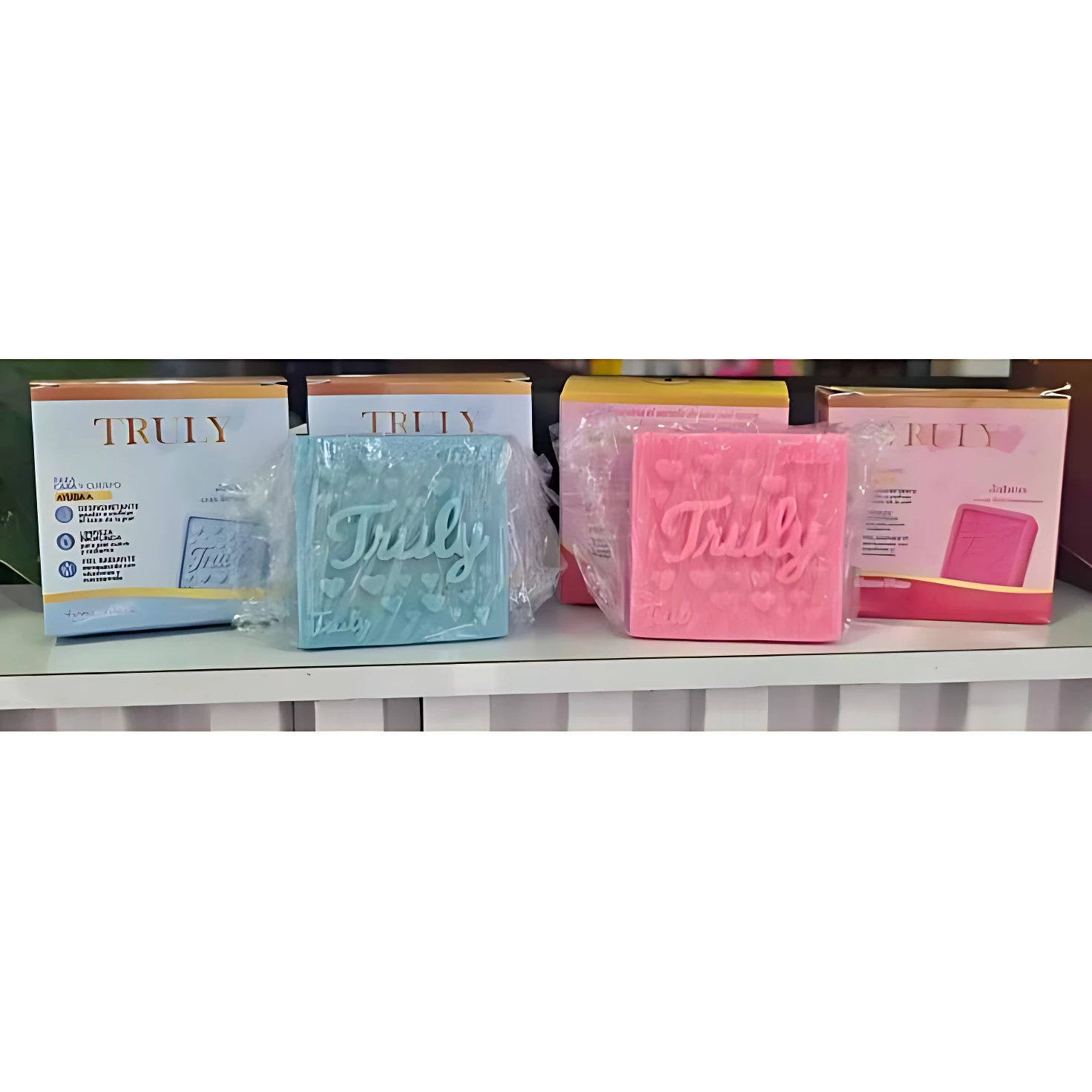 Set de dos jabones Truly en colores rosa y azul claro, con textura de puntos y logotipo en relieve, presentados junto a sus cajas originales sobre estante blanco.