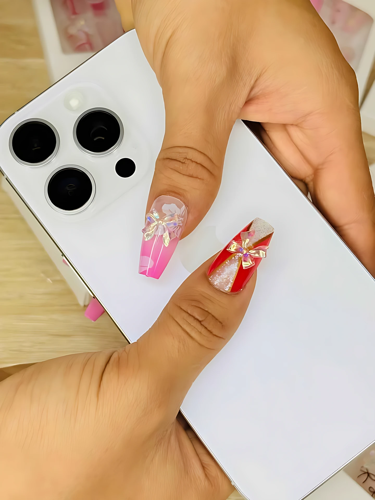 Mano sosteniendo teléfono blanco, mostrando uñas postizas largas con diseños de flores en tonos rosa y rojo sobre base blanca.