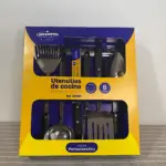 Pack de seis utensilios de cocina en acero inoxidable, con mango negro y cabezales metálicos, presentados en caja amarilla y azul con ventana transparente. Incluye espátula, cuchara, tenedor, espátula de silicona, colador y espátula plana.
