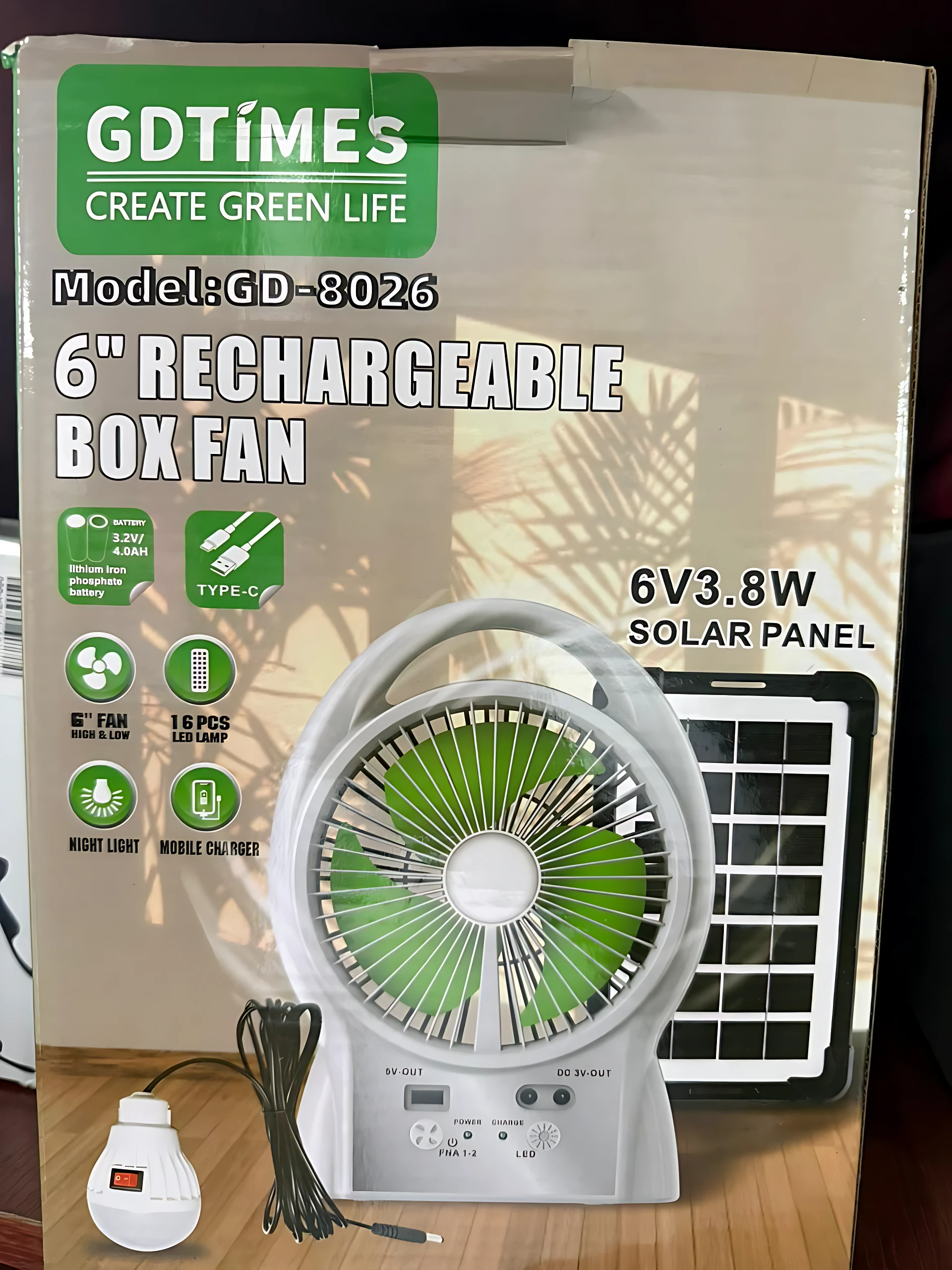 Ventilador portátil solar de 6 pulgadas con luz LED, panel solar integrado y cable de carga USB, sobre fondo de caja de producto.