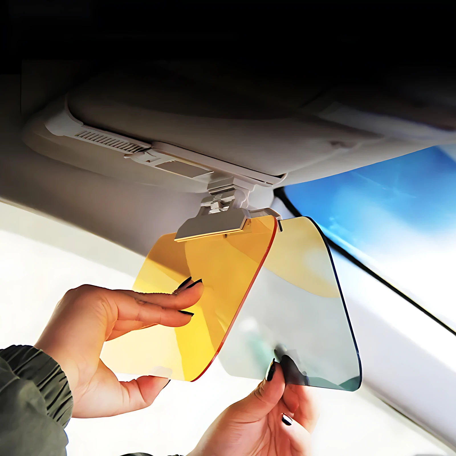Visera de coche con lentes intercambiables: una en tono ámbar y otra en gris claro, siendo ajustadas por manos frente al parabrisas para bloquear el sol.