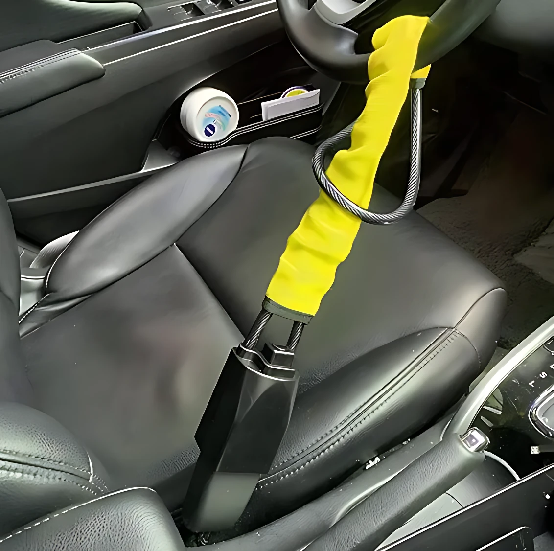 Volante Seguro Pro con bloqueo físico: funda amarilla con cable metálico enrollado, instalado en volante de auto negro, visiblemente bloqueado para disuadir robos.