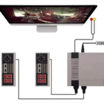 Miniconsola retro gris con dos mandos clásicos conectados, pantalla grande mostrando juego de acción, cable de alimentación y puertos visibles en lateral.