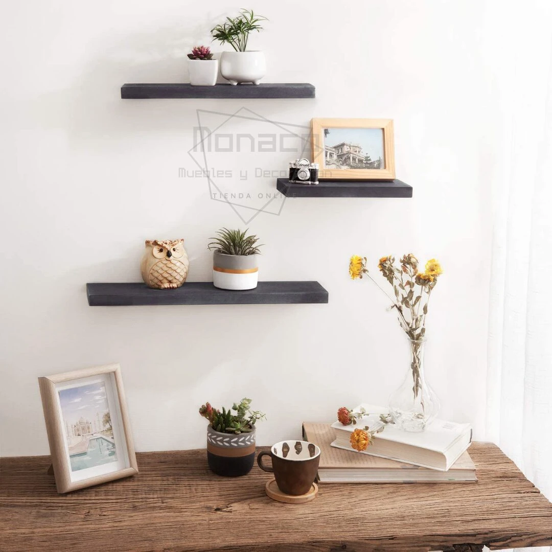 Tres repisas flotantes de madera oscura en pared blanca, exhibiendo plantas, marcos y objetos decorativos.