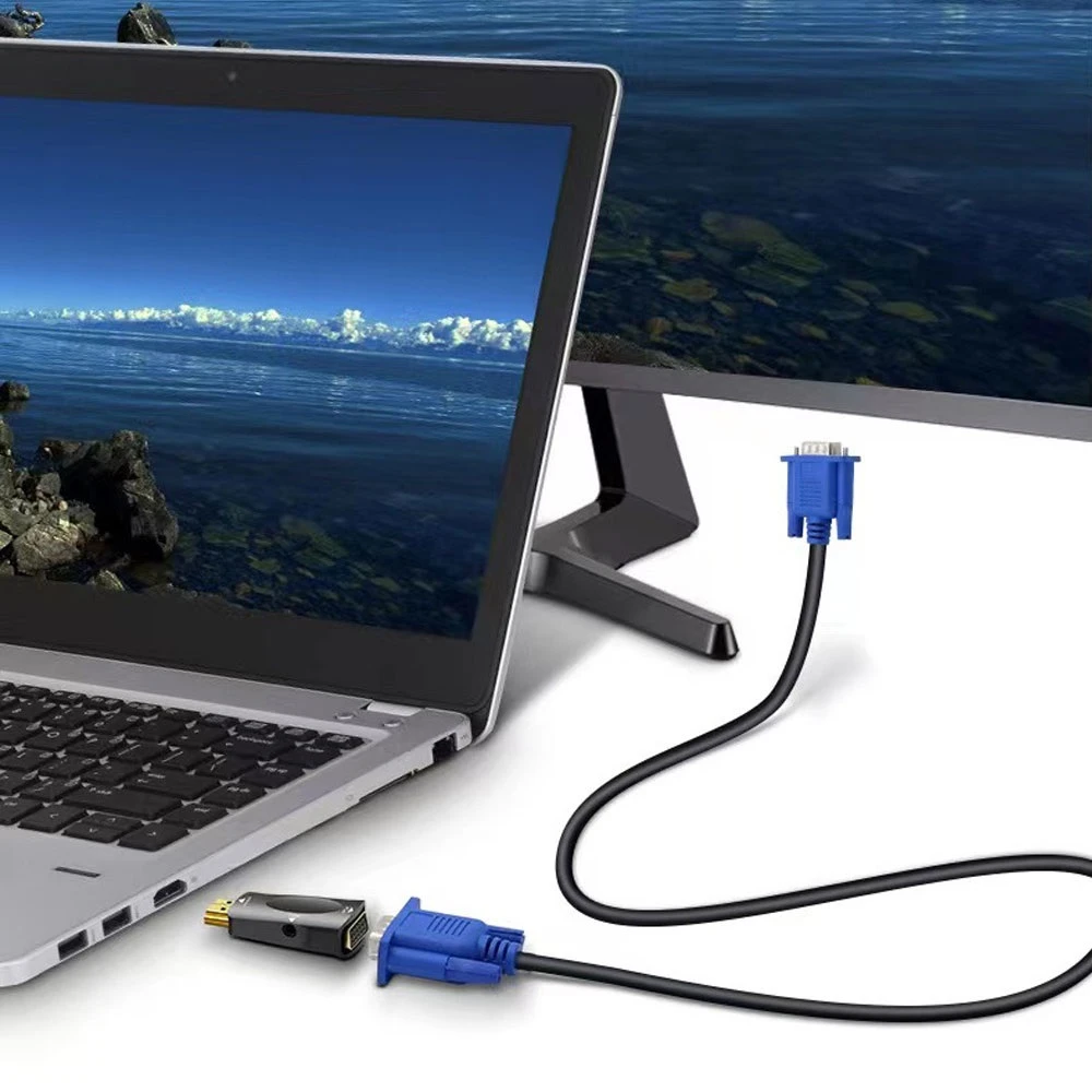 Adaptador HDMI a VGA azul con cable negro, conectado a laptop plateada y monitor externo, mostrando pantalla de paisaje costero. Incluye conector dorado y azul.