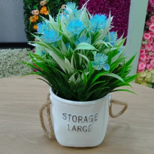 Bonsái artificial en maceta blanca con asas de cuerda, flores azules y follaje verde sobre mesa de madera.