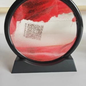 Reloj de arena circular con base negra, esfera roja y blanca con textura de arena en movimiento. Incluye código QR en la parte frontal.