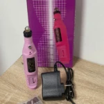 Kit de pulidor de uñas eléctrico en color rosa, con dos unidades, cargador y caja de accesorios, sobre superficie de madera.