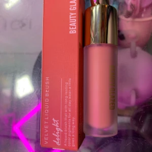 Rubor líquido Delight en presentación con aplicador de gota, color rosa pastel, junto a su caja roja con texto vertical. Producto de maquillaje para realzar el tono natural de la piel.