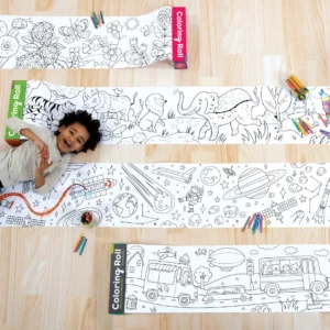 Niño sonriendo sobre rollo de papel para colorear con dibujos de animales, espacio y ciudad, acompañado de lápices de colores.