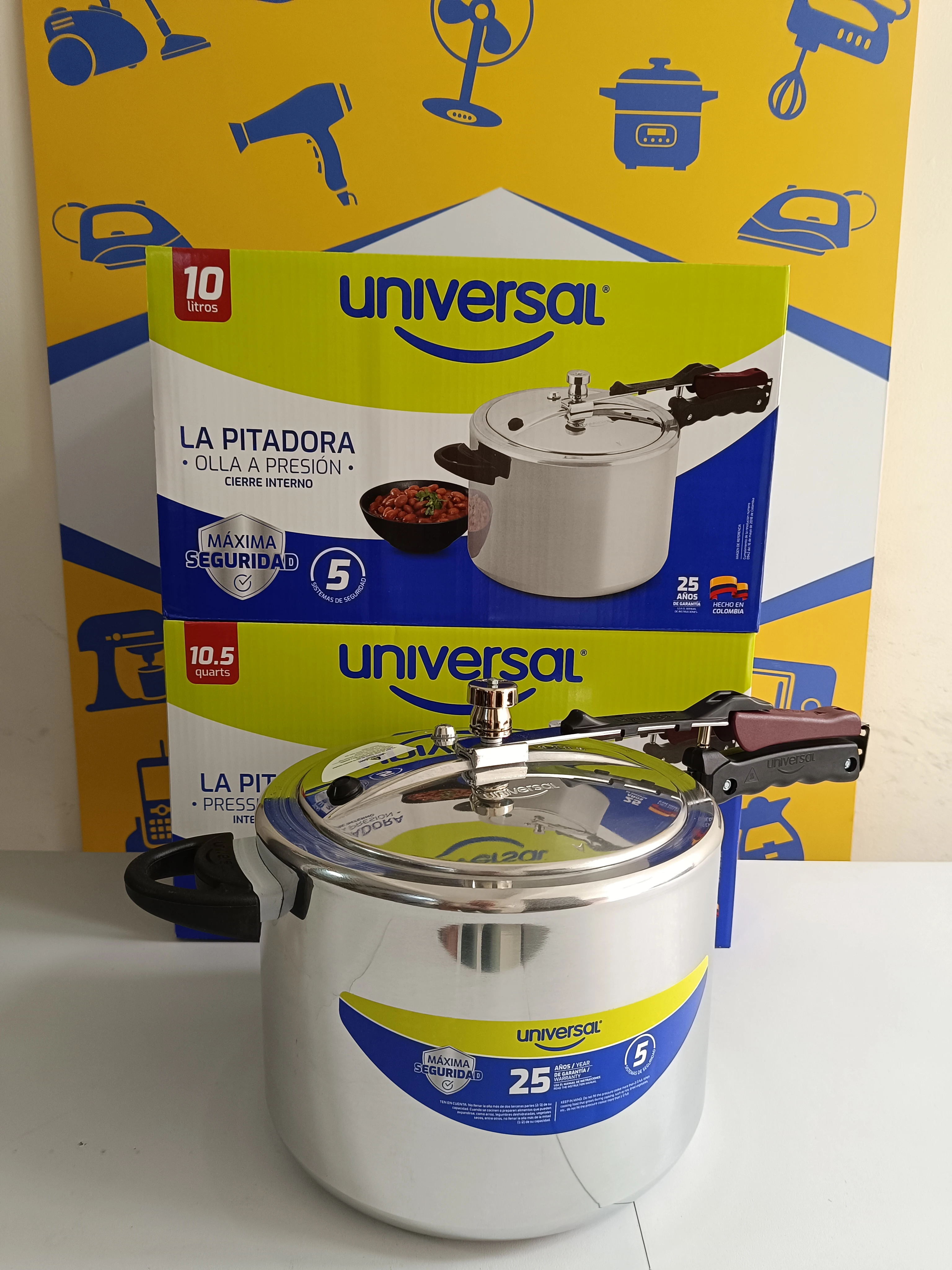 Olla a presión de aluminio Universal de 10 litros, con tapa metálica y mango negro, sobre caja amarilla con ilustraciones de electrodomésticos.