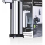 Dispensador automático de jabón en acero inoxidable con sensor infrarrojo, base negra y empaque visible al fondo.