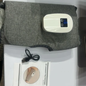 Masajeador de piernas con compresión de aire y calor profundo, en color gris claro, sobre tela texturizada. Incluye control digital blanco con pantalla azul, cable USB y manual de instrucciones.