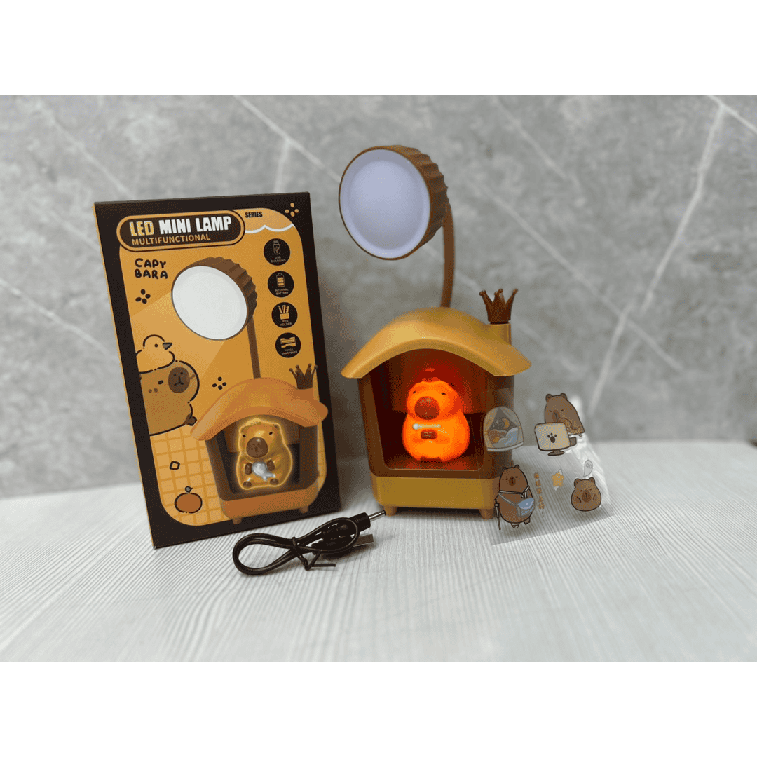 Lámpara LED multifuncional en forma de casa de capibara, color marrón claro, con luz cálida encendida, junto a su empaque y accesorios incluidos.