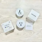 Vista superior de un adaptador inteligente blanco con enchufes, acompañado de su caja, manual y logotipos de Alexa y Google.