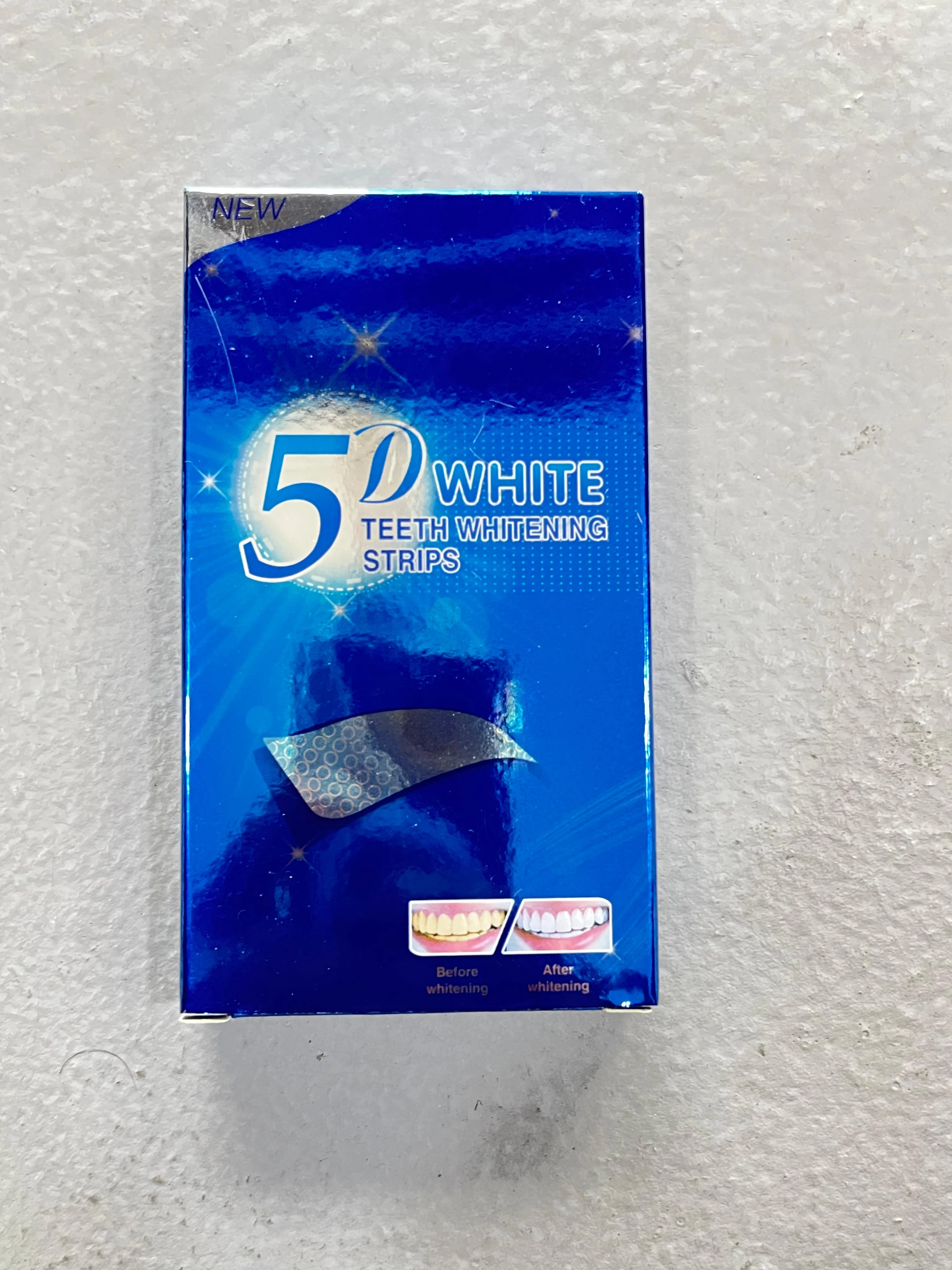 Caja azul de cinta blanqueadora 5D, con etiqueta de "NEW" en la esquina superior izquierda. Muestra una tira adhesiva plateada y dos imágenes comparativas de dientes antes y después del uso.