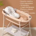 Bañera plegable color crema con base metálica blanca y cojín ergonómico estampado, sobre estante inferior con toallas y pato de goma.