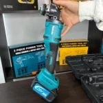 Pulidora inalámbrica Makita 128V brushless en color turquesa y negro, con batería incluida, siendo sostenida por una mano sobre estantería con cajas del kit de dos piezas.