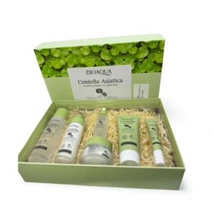 Caja abierta de color verde claro con cinco productos de skincare en su interior, sobre relleno de paja. Incluye botellas y tubos con etiquetas que indican Centella Asiática, diseñados para piel grasa y acné.