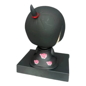 Figura chibi de Itachi Uchiha con cabeza negra y detalles rojos, sobre base rectangular con nubes rosas; soporta teléfono verticalmente.