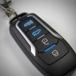 Llave remota negra con cuatro botones iluminados en azul para control remoto de alarma y localización de vehículo.